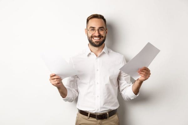 Smiling man in a white shirt and glasses holding papers in both hands, standing against a white background