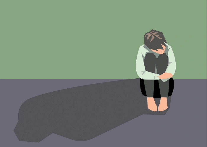 a person sitting alone on the floor hugging their knees with head down